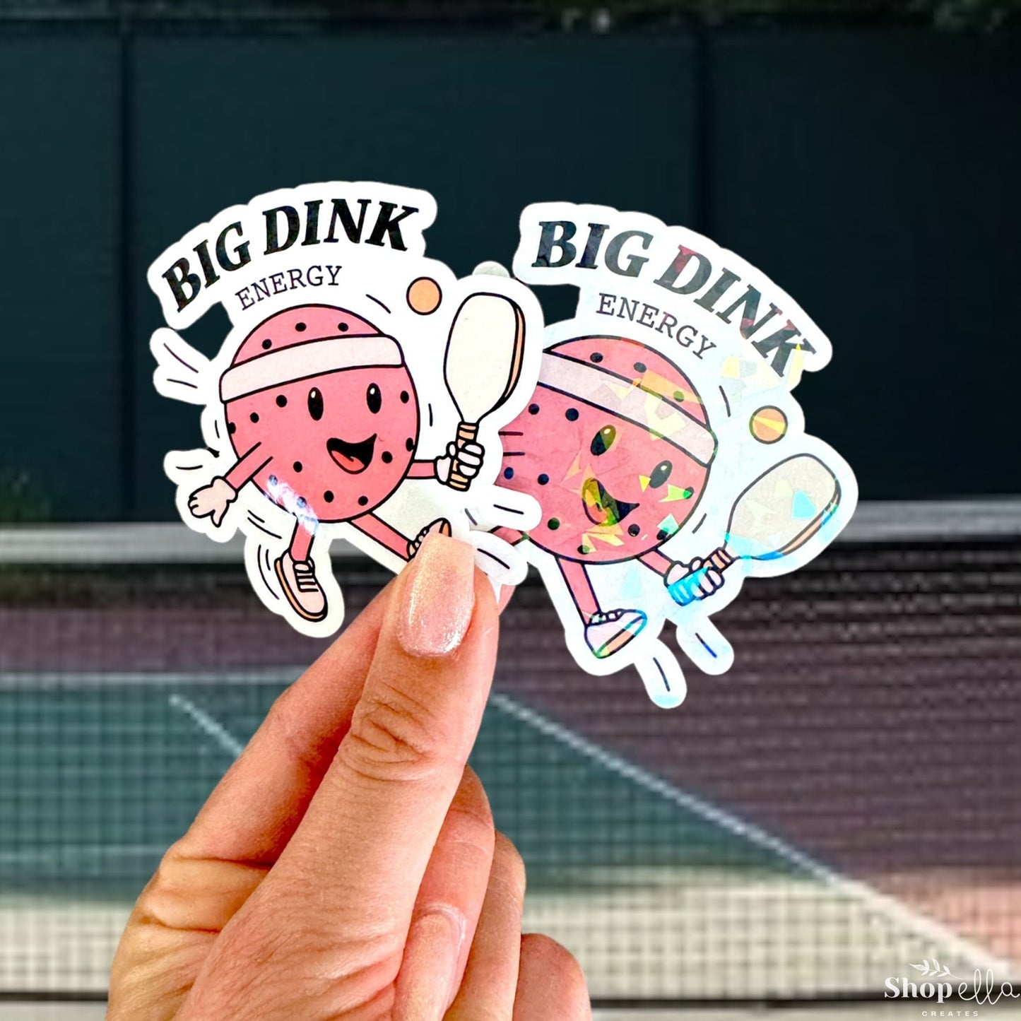a hand holding up two stickers with a tennis court in the background