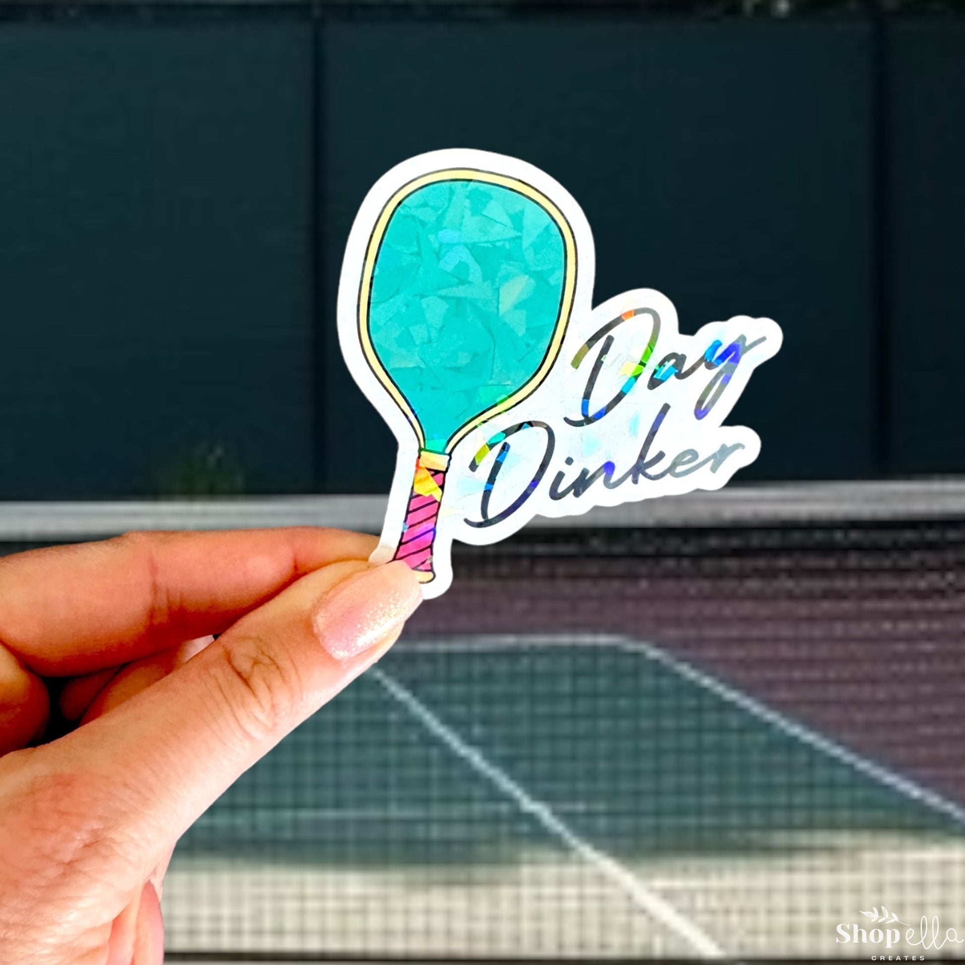 a hand holding up a sticker with a tennis court in the background