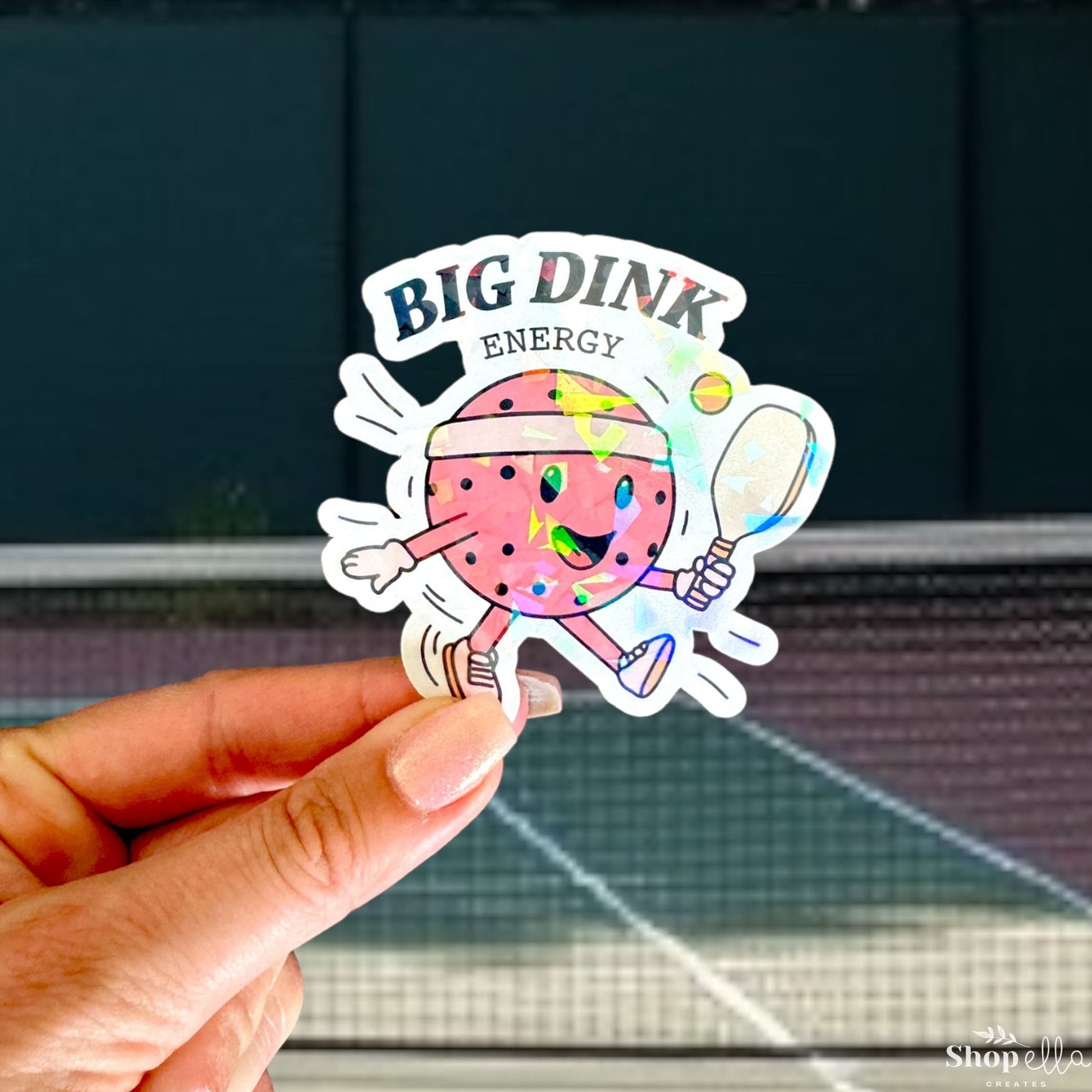 a hand holding a sticker with a picture of a tennis ball and rac