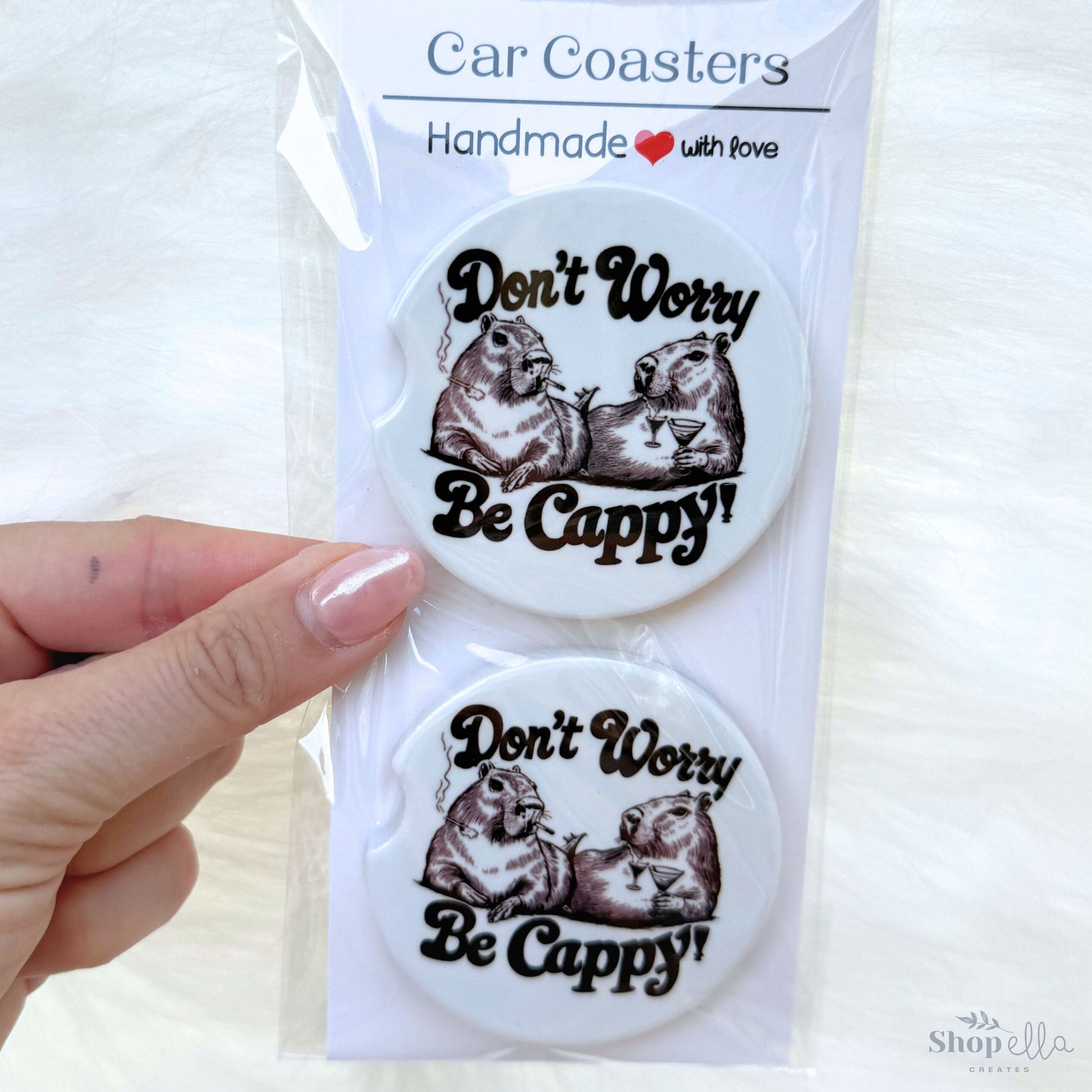 a pair of car coasters that say don't worry be cappy with a pic of two capybaras drinking margaritas and smoking. has a retro vibe