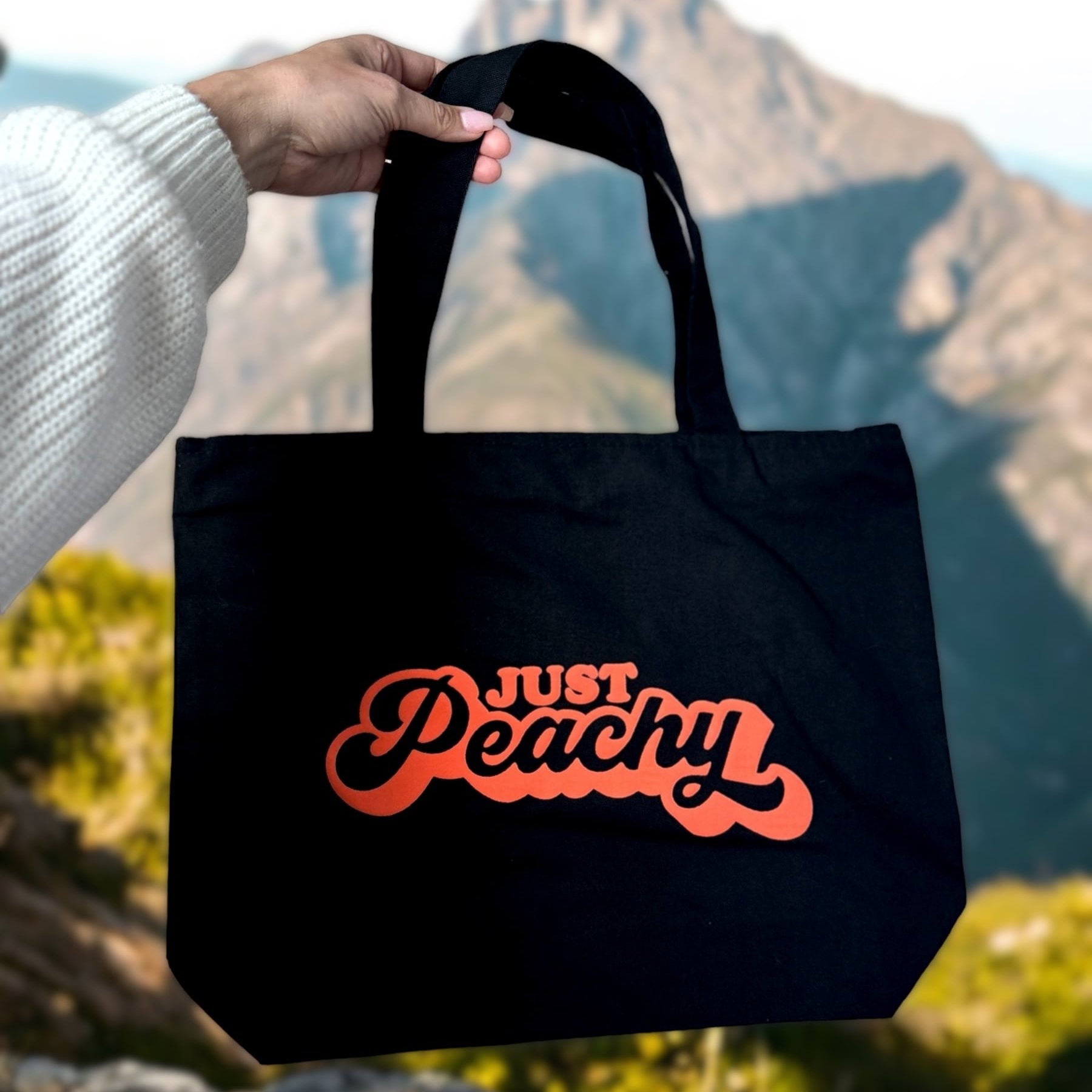hand holding just peachy black tote bag zippered