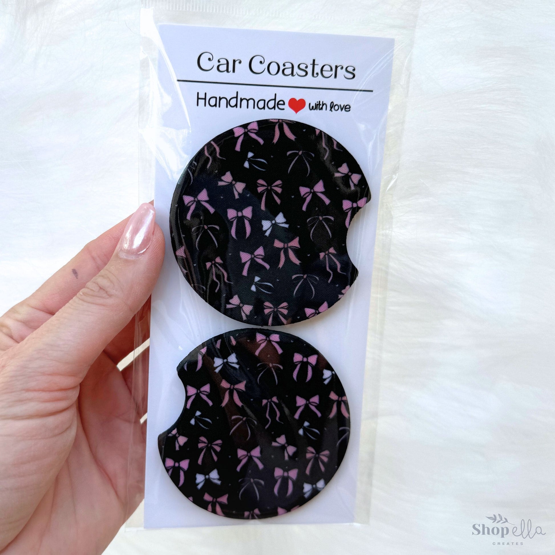 a package of car coasters with pink and beige bows on black background