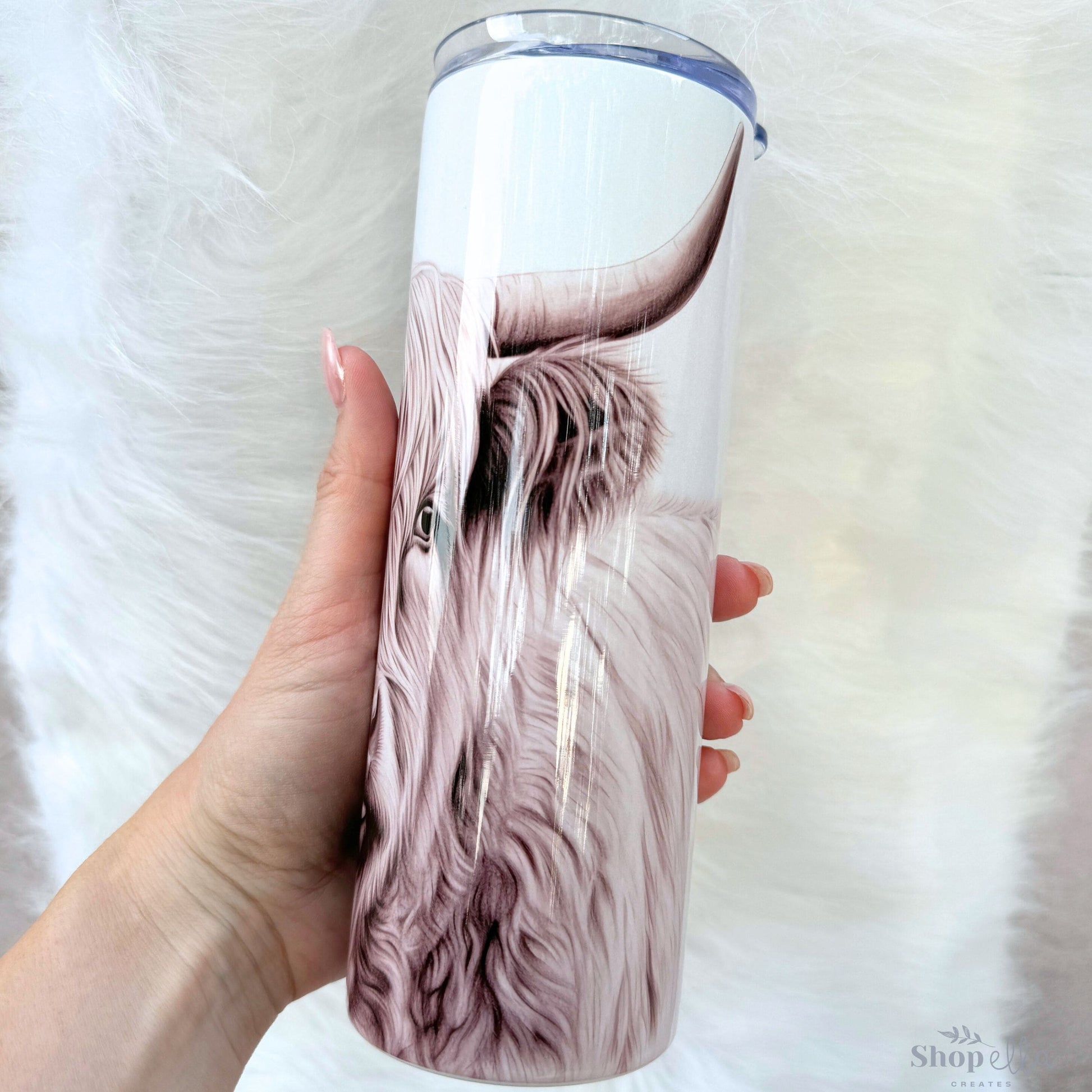 a hand holding a cup with a picture of a long haired cow on it